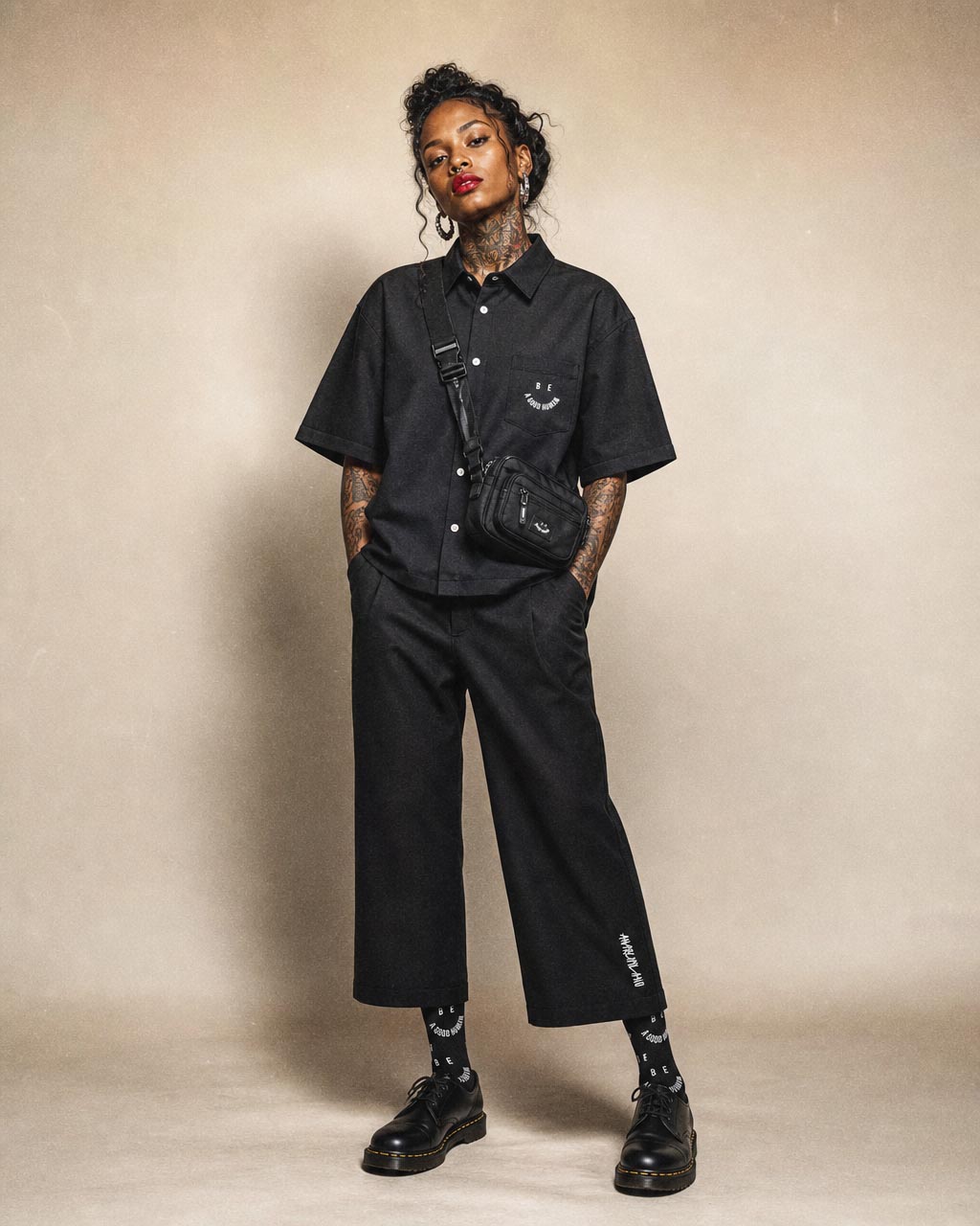 Person in all black streetwear with a crossbody bag standing with hands in pockets and a confident tilt