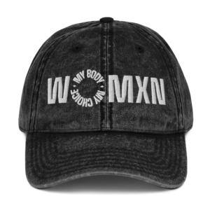 Washed black baseball cap with large white 'WMXN' lettering and a circular surrounding slogan embroidered on the front panel.